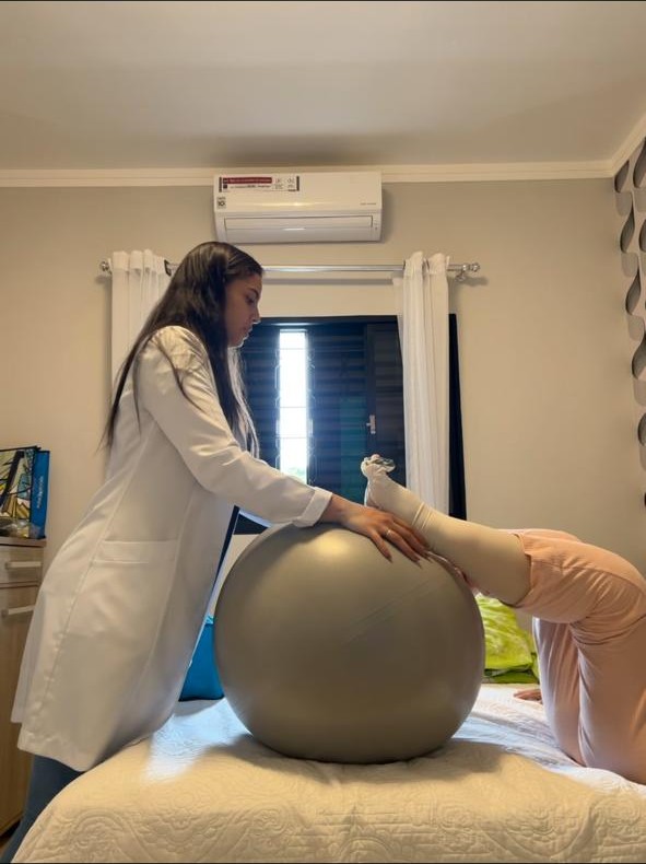 Bruna Kramer conduzindo exercício terapêutico com bola durante fisioterapia domiciliar no Cambuí